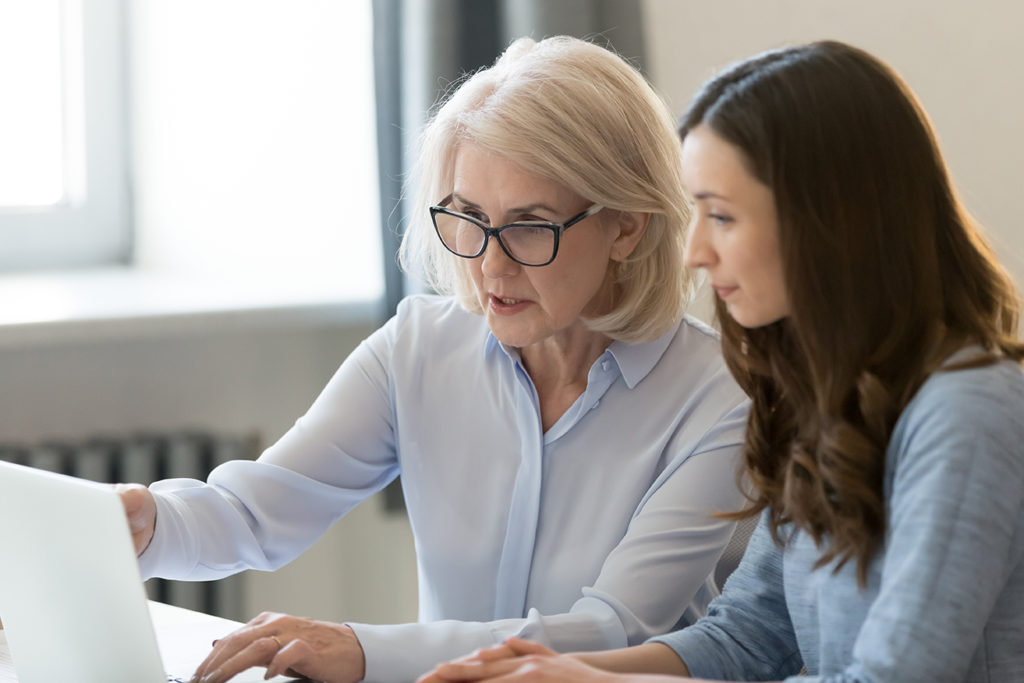 Serious old mentor teaching intern or student pointing at laptop