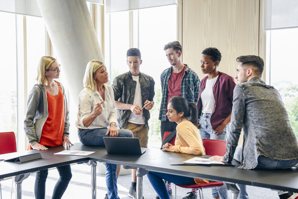 Six college students listening to mature female lecturer with laptop in classroom